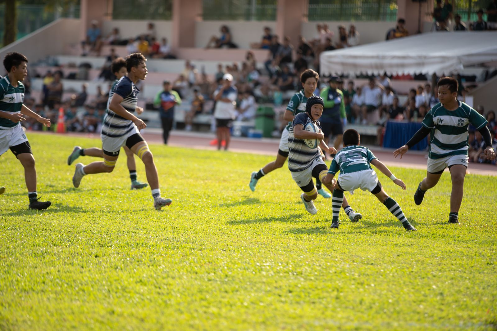 A junior rugby match, one player running with the ball as others chase